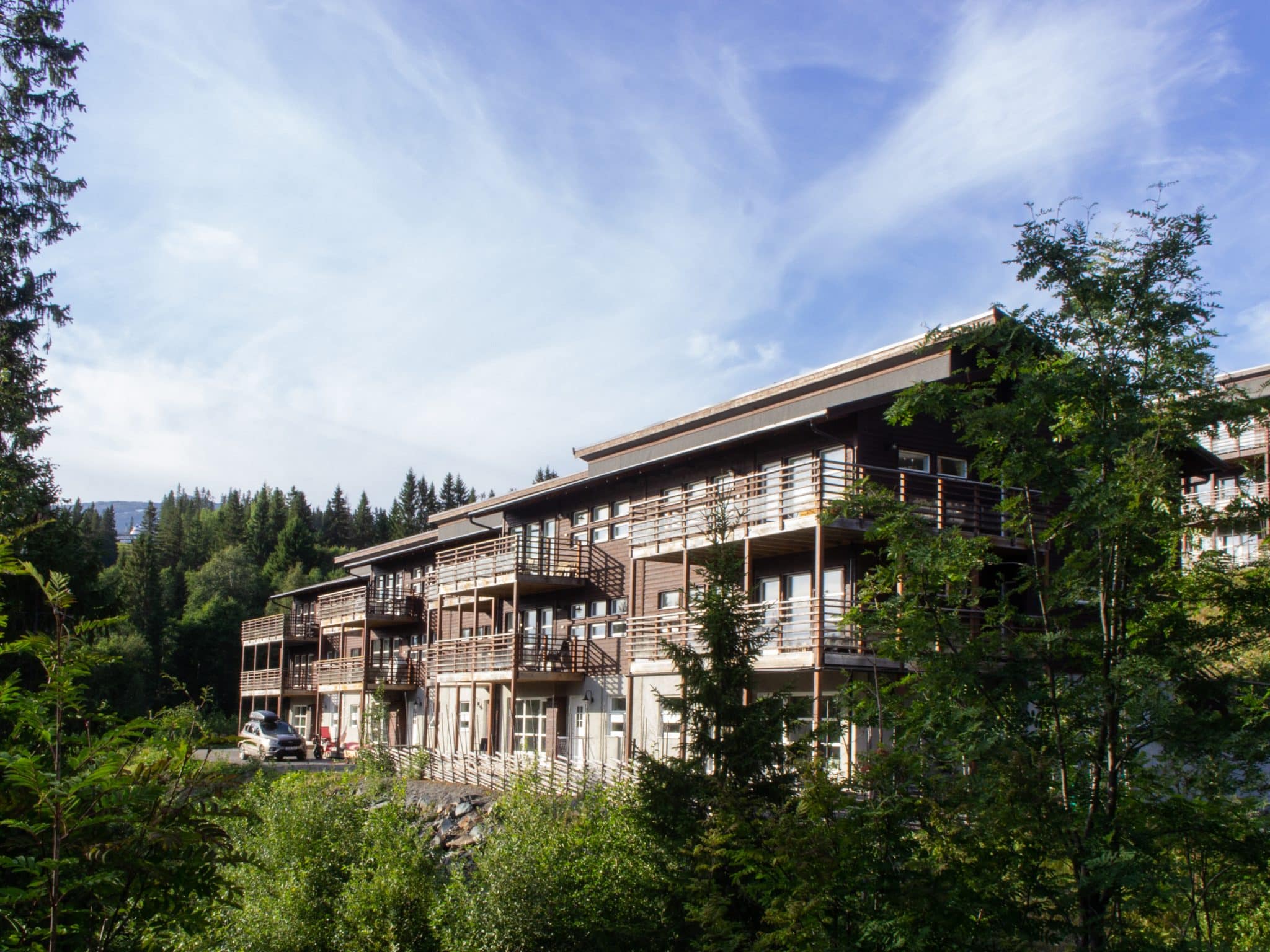 Bear Lodge in Åre Björnen, a brown strip of property with balconies in a green and leafy environment against a blue summer sky.