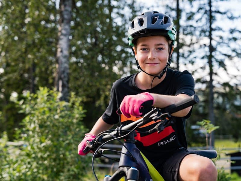 Pojke med hjälm på en MTB-cykel i skogen på sommaren