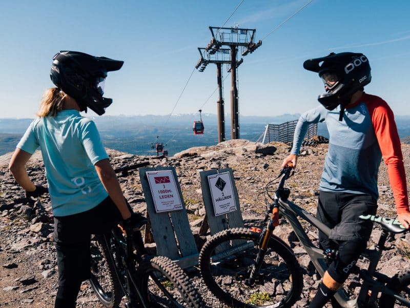 Två downhill-cyklister i hjälm på Åreskutan i sommarsol