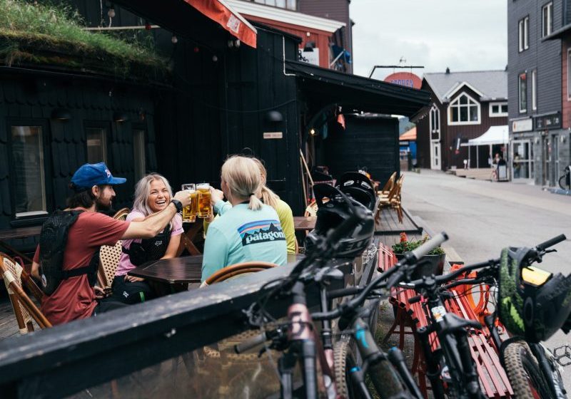 Ett glatt kompisgäng skålar på en uteservering i Åre, intill har de parkerat sina MYB-cyklar